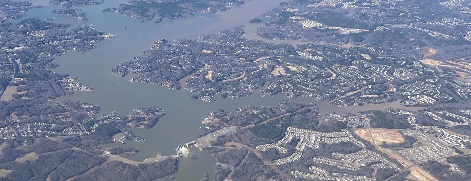 Aerial view of Lake Wylie in winter, with Wylie Dam near the bottom and wooded, house-lined peninsulas of the Tega Cay shoreline reaching into the water